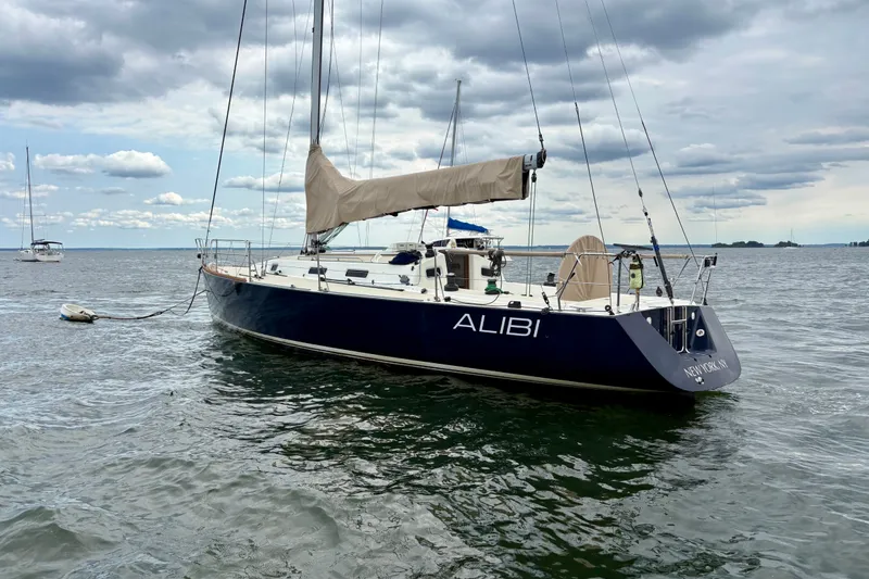 Slide: The Image of Sailboat J/120 from 2000 named "ALIBI" anchored on a calm sea under cloudy skies. - 2
