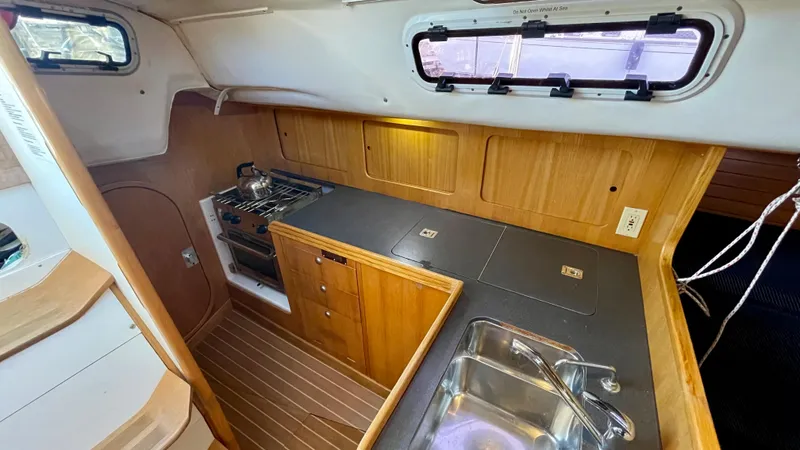 Slide: The Image of Interior view of a 2000 J/120 featuring a well-equipped galley and wood paneling. - 23
