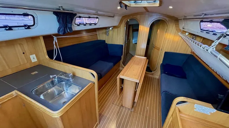 Slide: The Image of Interior of a 2000 J/120 with wood finish, blue seating, and a small kitchenette. - 21