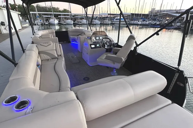 Slide: The Image of 2019 Harris Sunliner 240 pontoon boat interior with plush seating and illuminated controls at marina. - 32