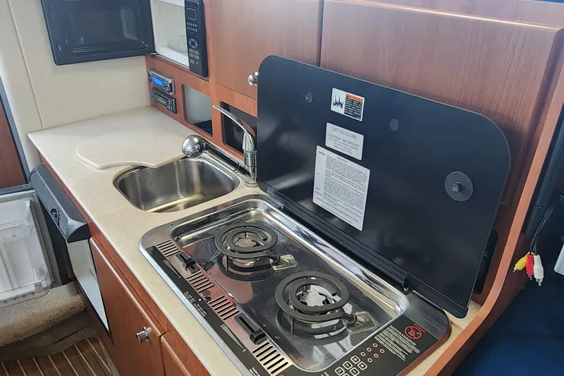 Slide: The Image of 2008 Bayliner 300 boat kitchen with stove, sink, and wooden cabinetry. - 12