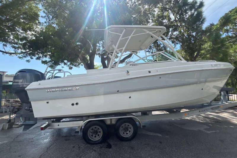 The Image of 2024 World Cat 230 SD boat on trailer, parked under trees, with Yamaha engine. - 1