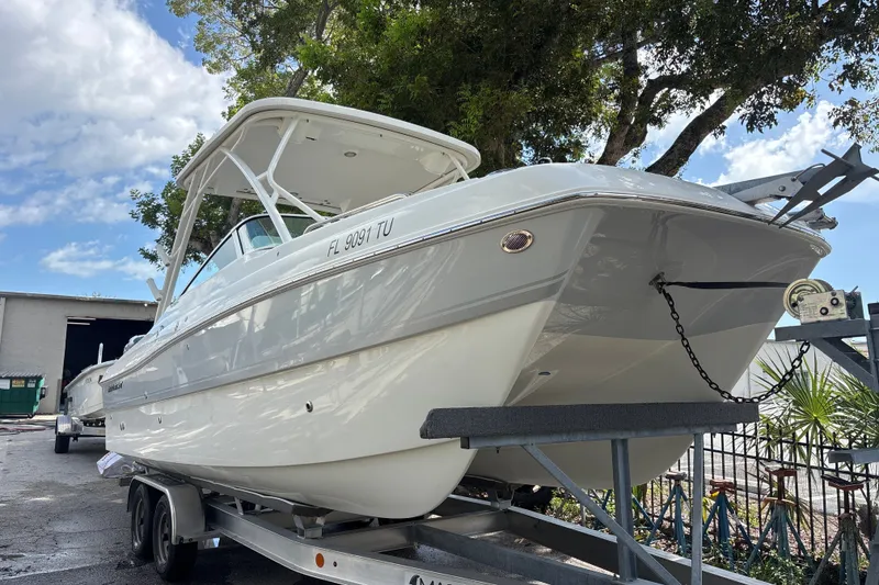 Slide: The Image of 2024 World Cat 230 SD boat on trailer, parked outdoors under a tree. - 2