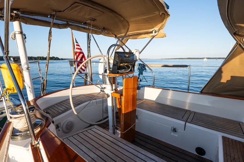 Slide: The Image of Sailboat cockpit with wooden deck, steering wheel, and American flag on calm water. - 16