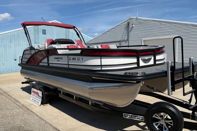 Slide: The Image of 2022 Bennington R 24 Quad Bench Bowrider on trailer, parked near blue building. - 1