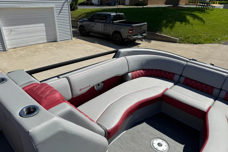 Slide: The Image of 2022 Bennington R 24 Quad Bench Bowrider with red and gray seating, parked near a garage. - 12