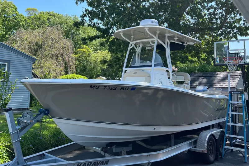 Slide: The Image of 2018 NauticStar 2302 Legacy boat on trailer, parked in a driveway with greenery. - 1