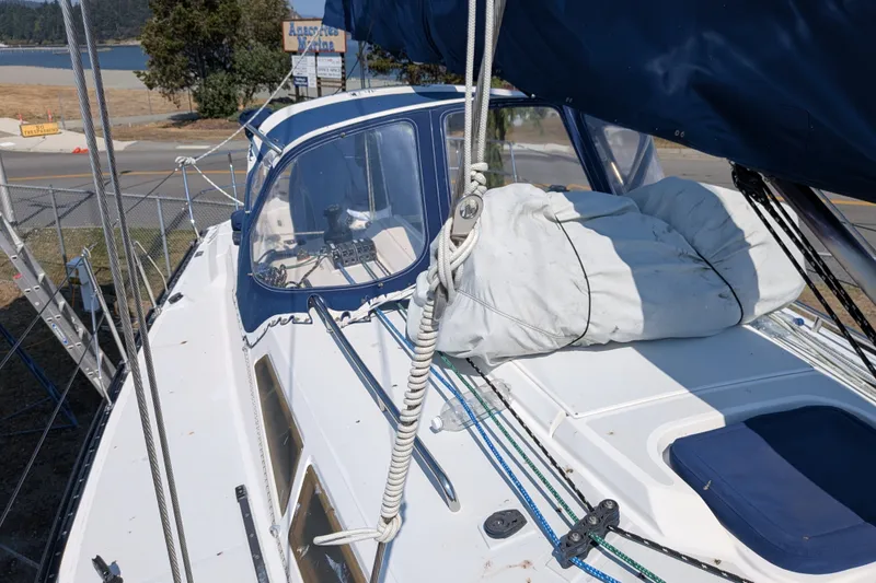 Slide: The Image of Sailboat deck of 2005 C&C 115, featuring ropes and covered equipment, docked near a scenic shoreline. - 24