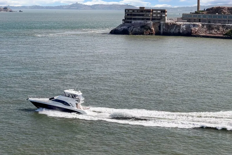 Slide: The Image of 2007 Sea Ray 58 Sedan Bridge cruising near a rocky shoreline and industrial building. - 14