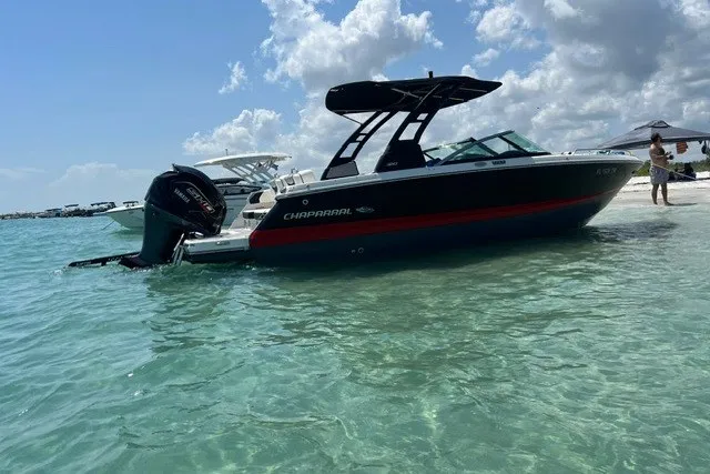Slide: The Image of 2024 Chaparral 250 OSX boat anchored in clear turquoise water near a sandy beach. - 2