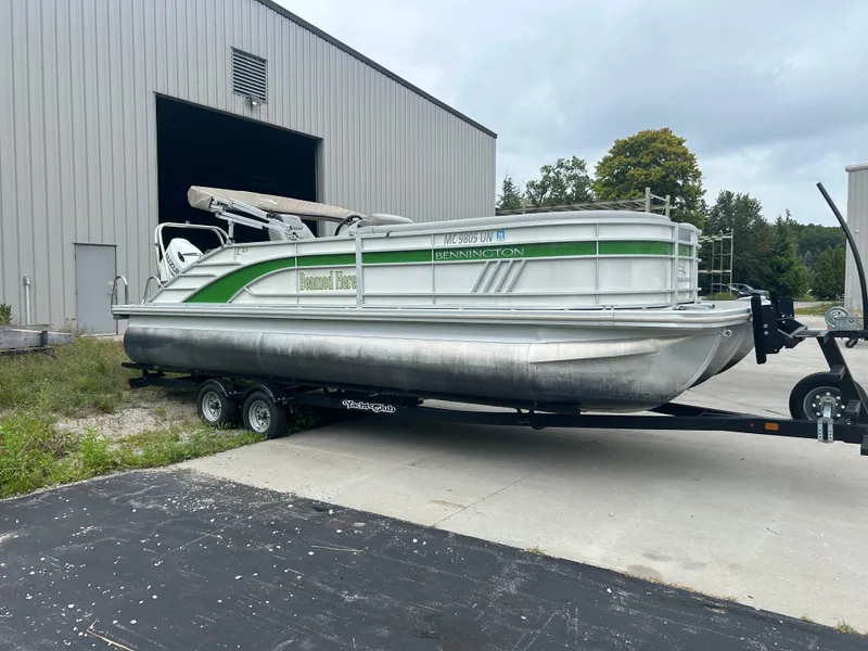 Slide: The Image of A 2021 Bennington 23LSBSD pontoon boat on a trailer outside a large building. - 3