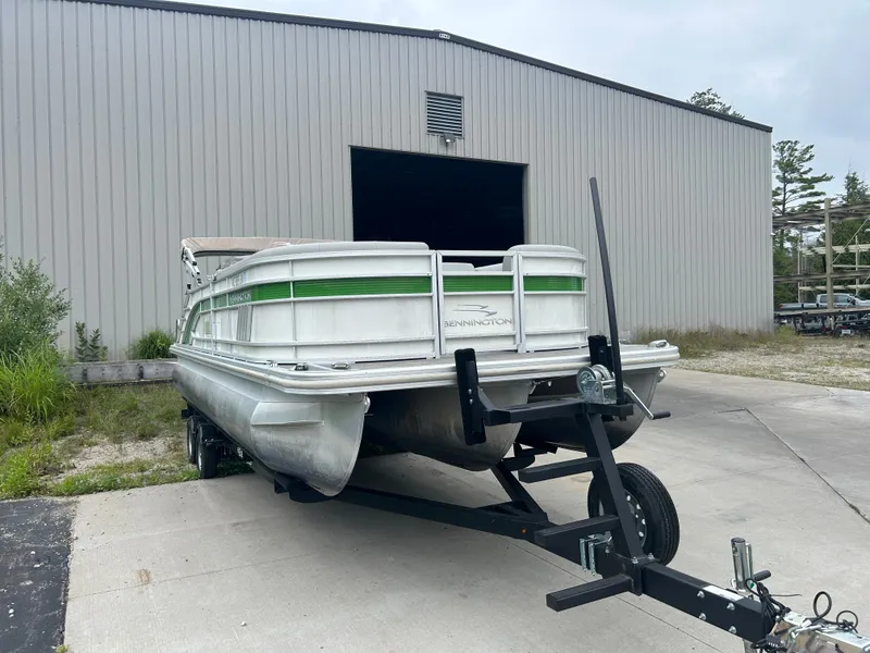 Slide: The Image of A 2021 Bennington 23LSBSD pontoon boat on a trailer in front of a large building. - 2