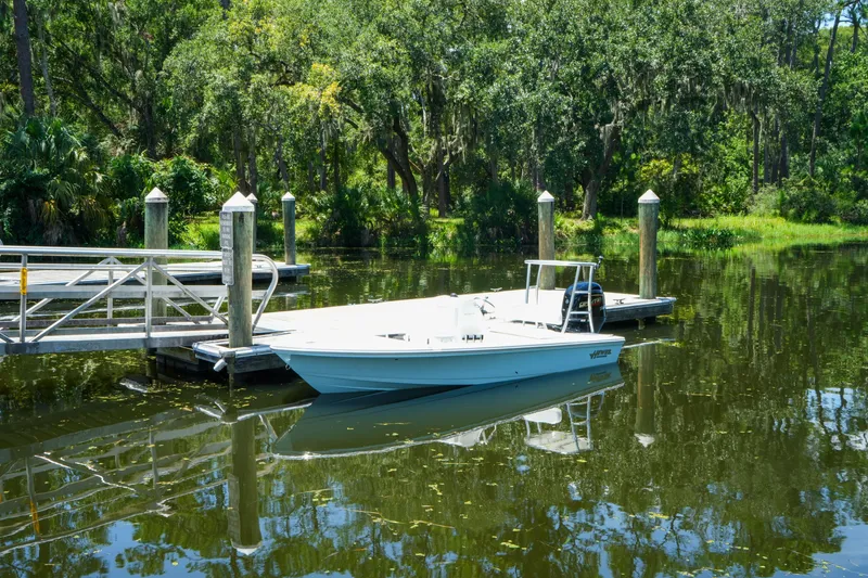 Slide: The Image of 2027 Hewes Redfisher 16 boat docked on a serene, tree-lined waterway. - 30