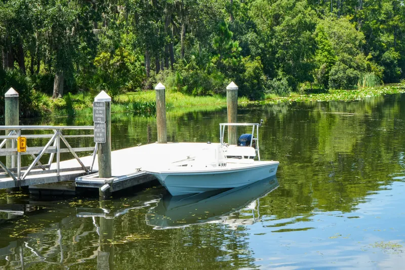 Slide: The Image of 2027 Hewes Redfisher 16 boat docked on a serene, tree-lined river. - 28