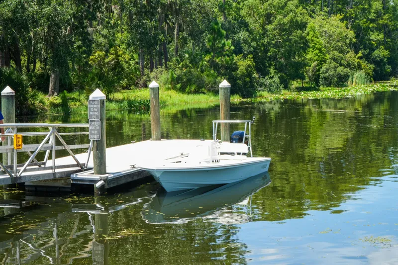 Slide: The Image of 2027 Hewes Redfisher 16 boat docked on a serene, tree-lined river. - 27