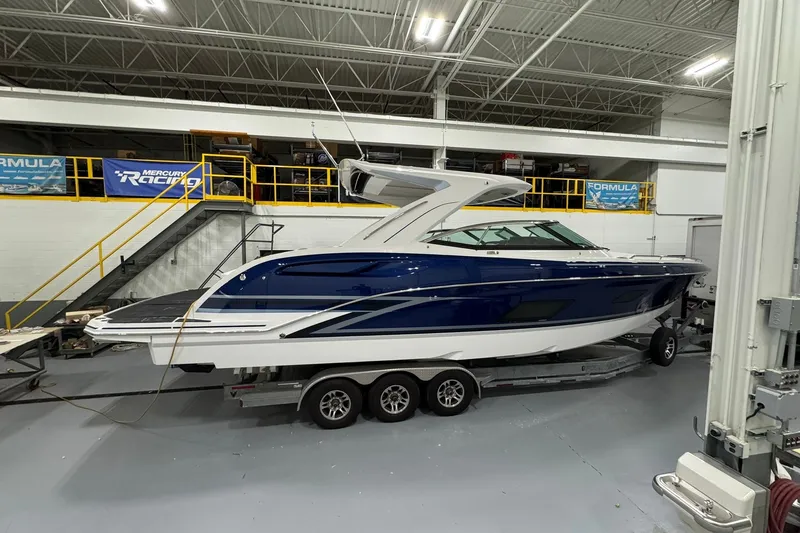Slide: The Image of 2026 Formula 360 Crossover Bowrider I/O in showroom, blue and white design, on trailer. - 2