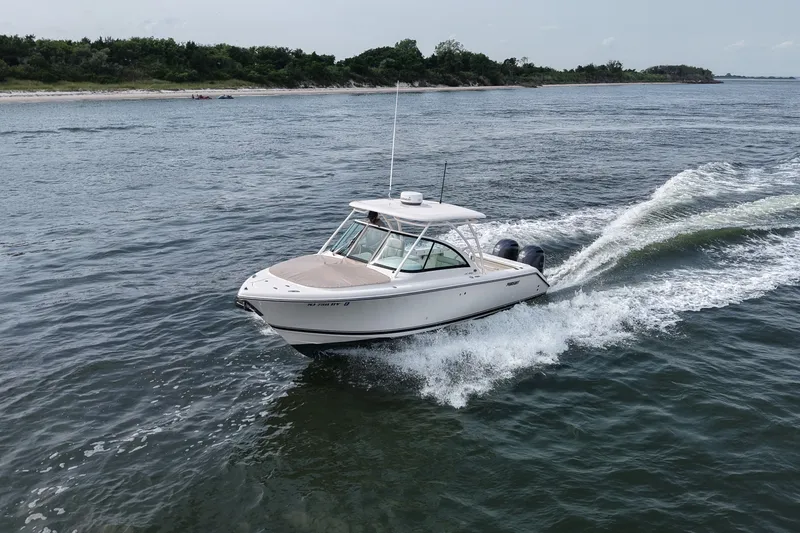 Slide: The Image of 2014 Pursuit DC 265 Dual Console boat cruising on open water near a shoreline. - 12
