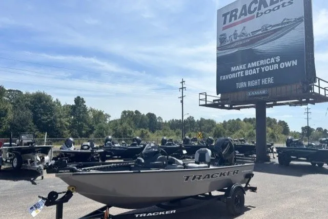 The Image of 2027 Tracker Super Guide V-16 SC boat displayed outdoors at dealership with promotional billboard. - 0