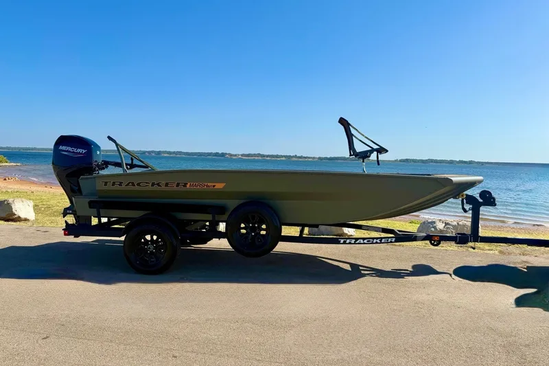 The Image of 2027 Tracker Grizzly 1756 T Marsh boat on trailer by a lake. - 0