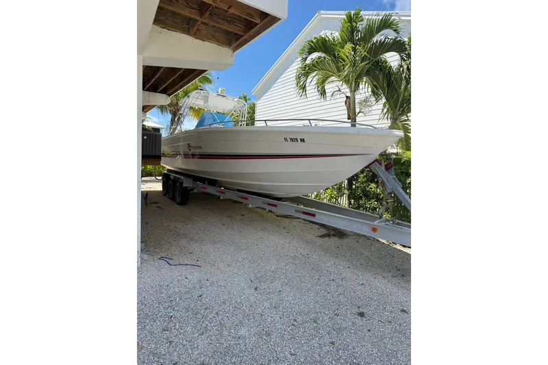 The Image of 1990 Avanti 33 boat on trailer, parked under a shelter with palm trees nearby. - 1