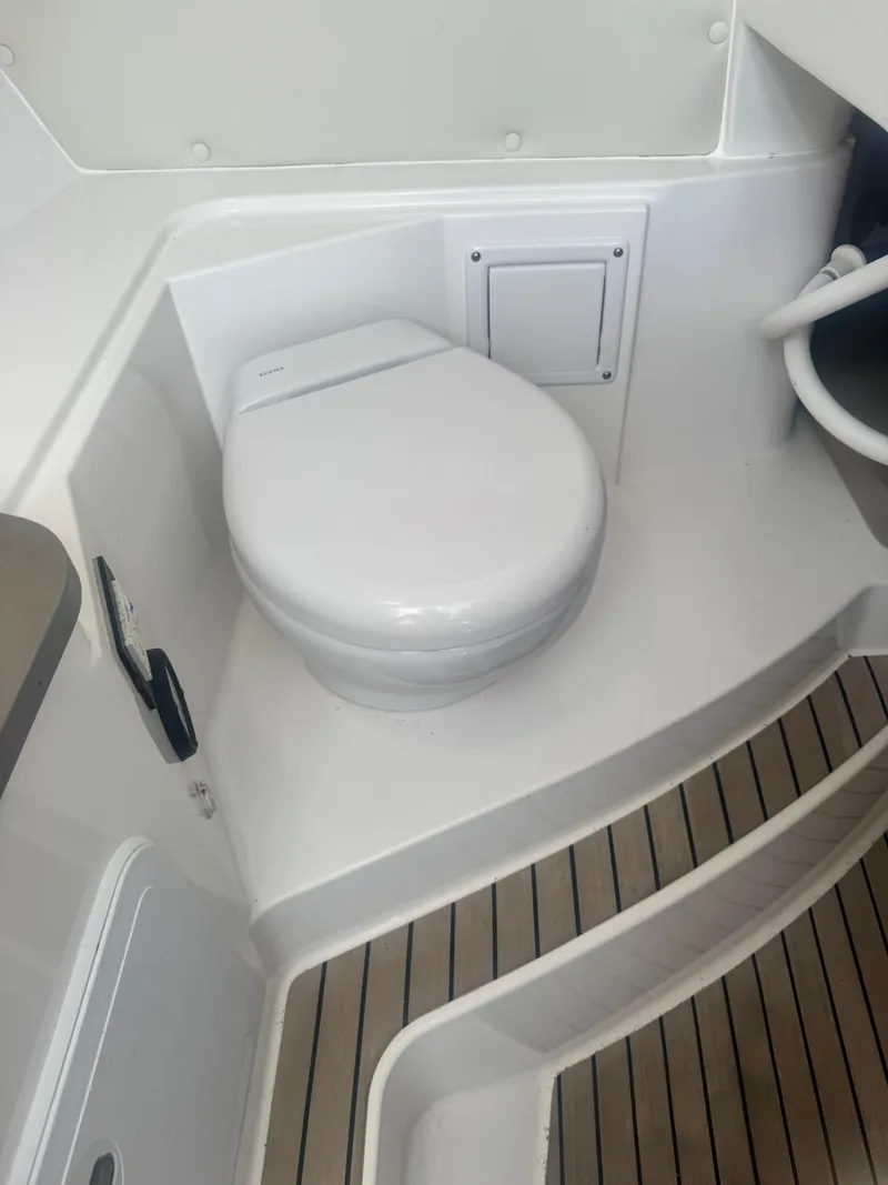Slide: The Image of The image shows a clean, white toilet in a boat bathroom with wooden flooring. - 25