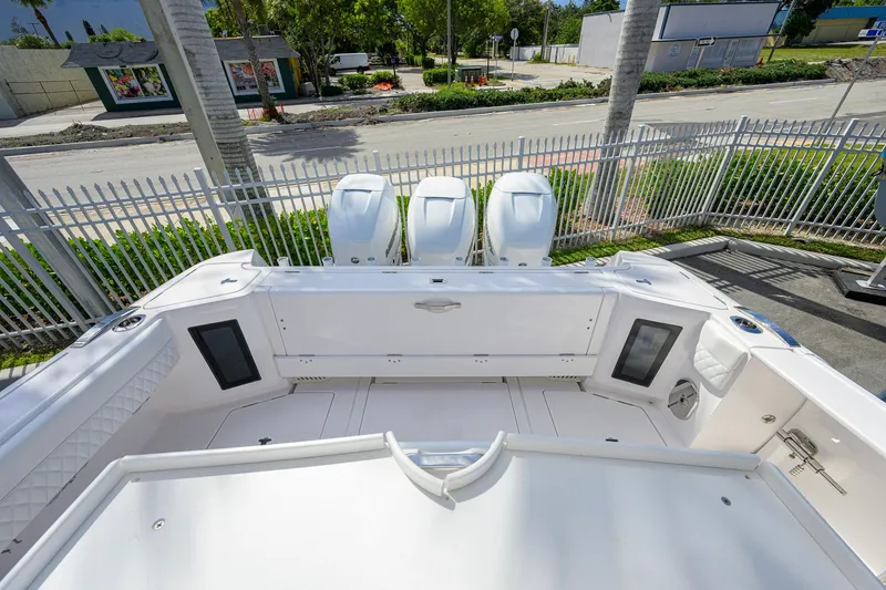 Slide: The Image of 2022 Intrepid 409 Valor boat deck with triple outboard engines, docked near a fence. - 30