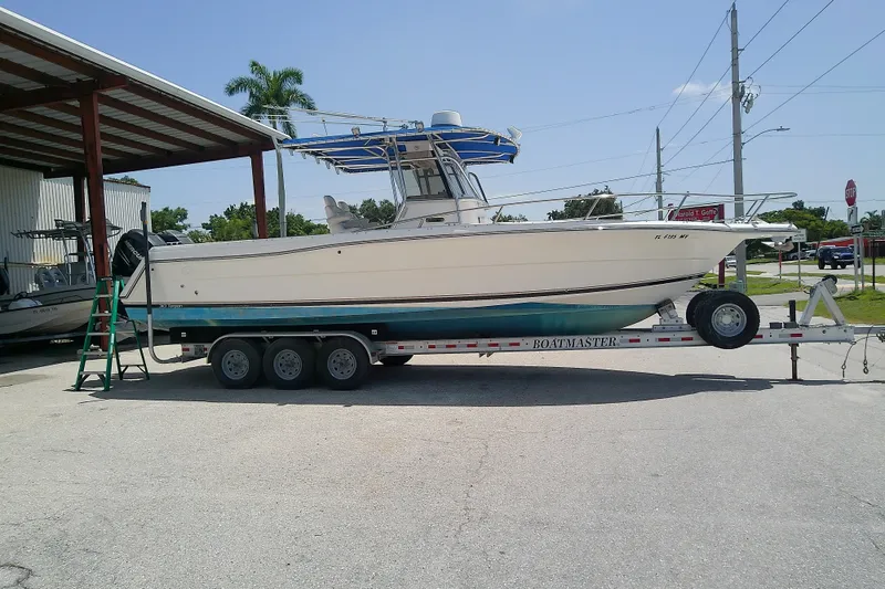 The Image of 2004 Stamas 310 Tarpon boat on trailer, parked outdoors under a metal canopy. - 0