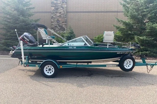The Image of 1994 DYNATRAK 160SS boat on trailer, parked outdoors near trees and brick wall. - 1