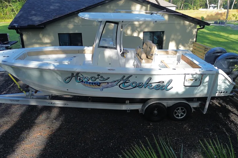 Slide: The Image of 2018 Sea Hunt Gamefish 27 boat on trailer, labeled "Hoo's Hooked," parked near a house. - 2