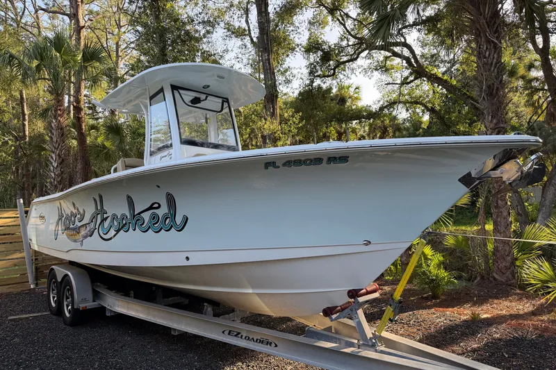 Slide: The Image of 2018 Sea Hunt Gamefish 27 boat on trailer, surrounded by trees. - 9