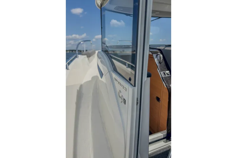 Slide: The Image of 2024 Nimbus Commuter 9 boat, side view with open cabin door, under clear blue sky. - 11