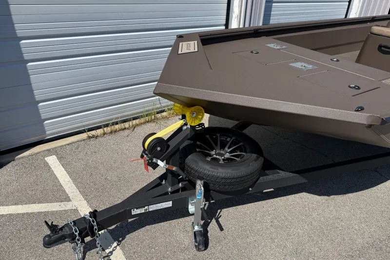 Slide: The Image of Trailer of 2027 Avid 20 Rogue CC boat parked on pavement near a garage. - 5