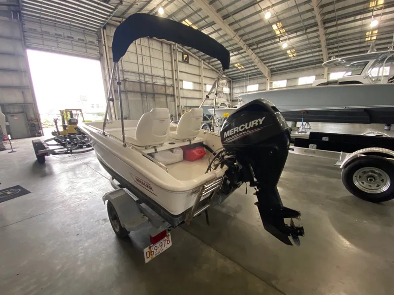 Slide: The Image of A 2017 Boston Whaler 130 Super Sport with a Mercury outboard motor in a warehouse. - 1