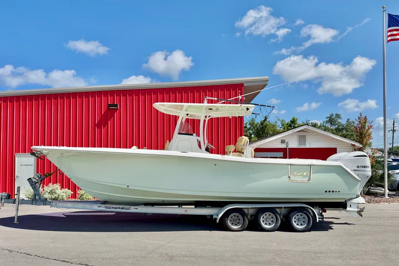 The Image of 2016 Sea Hunt Gamefish 30 boat on trailer, parked near red building under blue sky. - 0