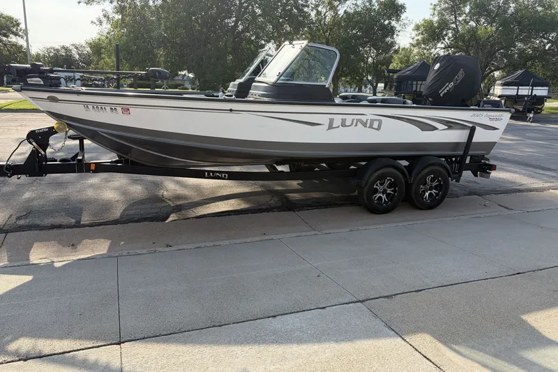 Slide: The Image of 2019 Lund 2025 Impact XS boat on trailer, parked outdoors. - 2