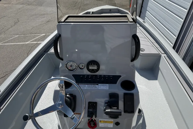 Slide: The Image of 2027 Avid 23 Mag boat console with steering wheel and gauges in a marina setting. - 17