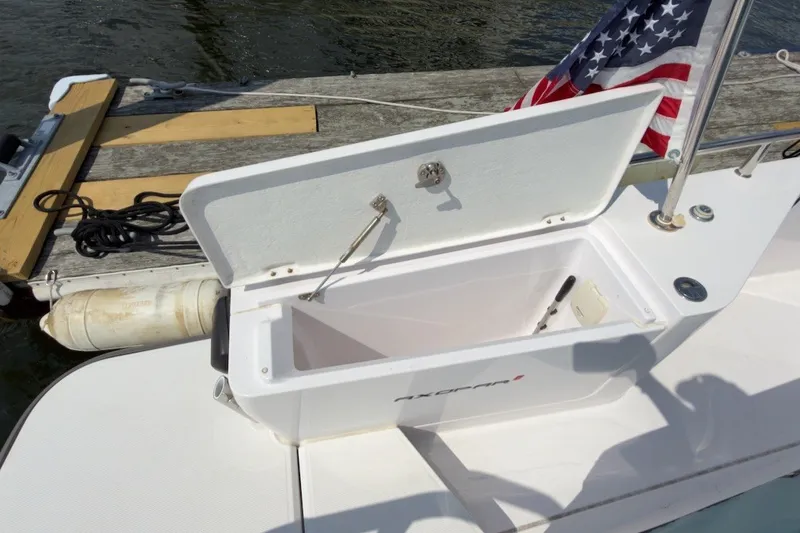 Slide: The Image of Open storage compartment on 2023 Axopar 28 Cabin boat, docked with American flag visible. - 43