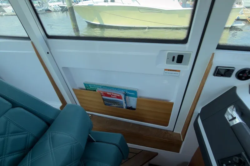 Slide: The Image of 2023 Axopar 28 Cabin interior with teal seating and window view of marina. - 32