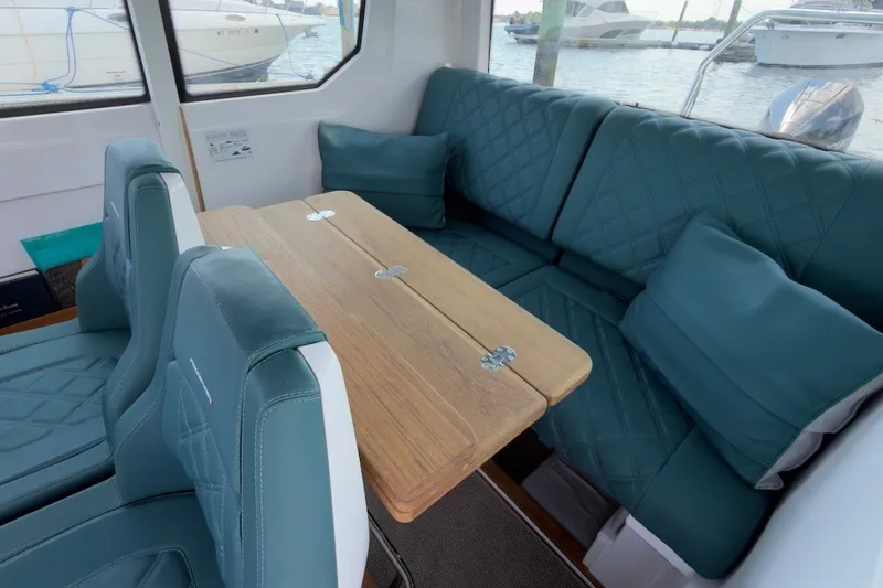 Slide: The Image of 2023 Axopar 28 Cabin interior with teal seating and wooden table, docked by the water. - 16