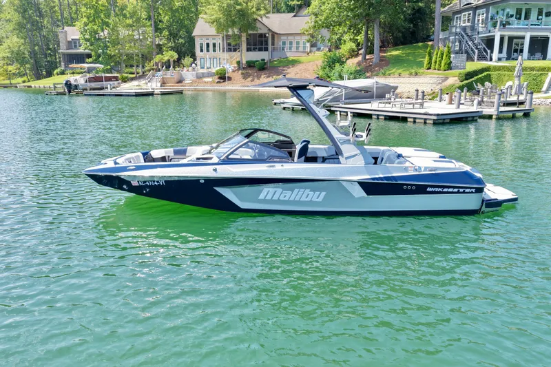 Slide: The Image of 2022 Malibu Wakesetter 23 MXZ boat on a serene lake near docks and houses. - 3