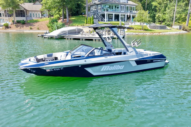 Slide: The Image of 2022 Malibu Wakesetter 23 MXZ boat on a serene lake near luxury homes. - 2