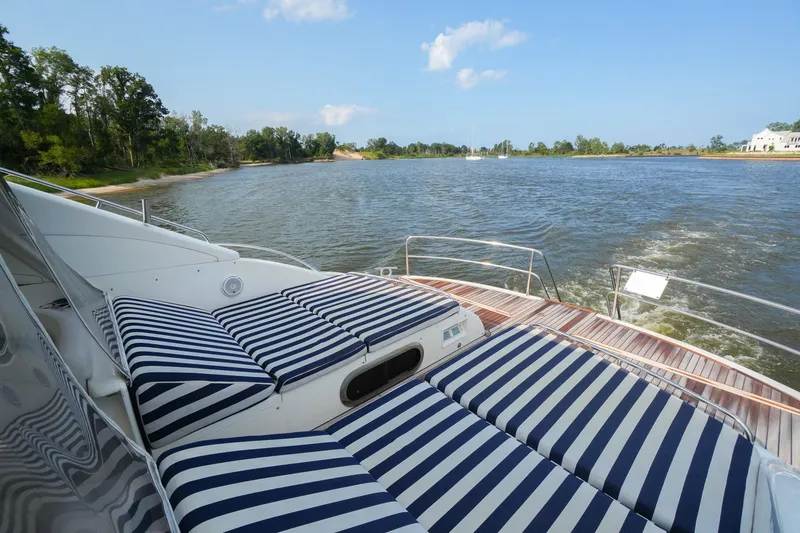Slide: The Image of 2001 Viking Sport Cruisers V65 yacht with striped sun loungers on deck, cruising on a scenic river. - 16