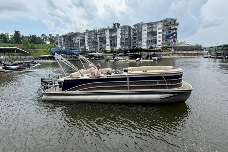 Slide: The Image of 2013 Harris Solstice 240 pontoon boat on a lake near waterfront buildings. - 2