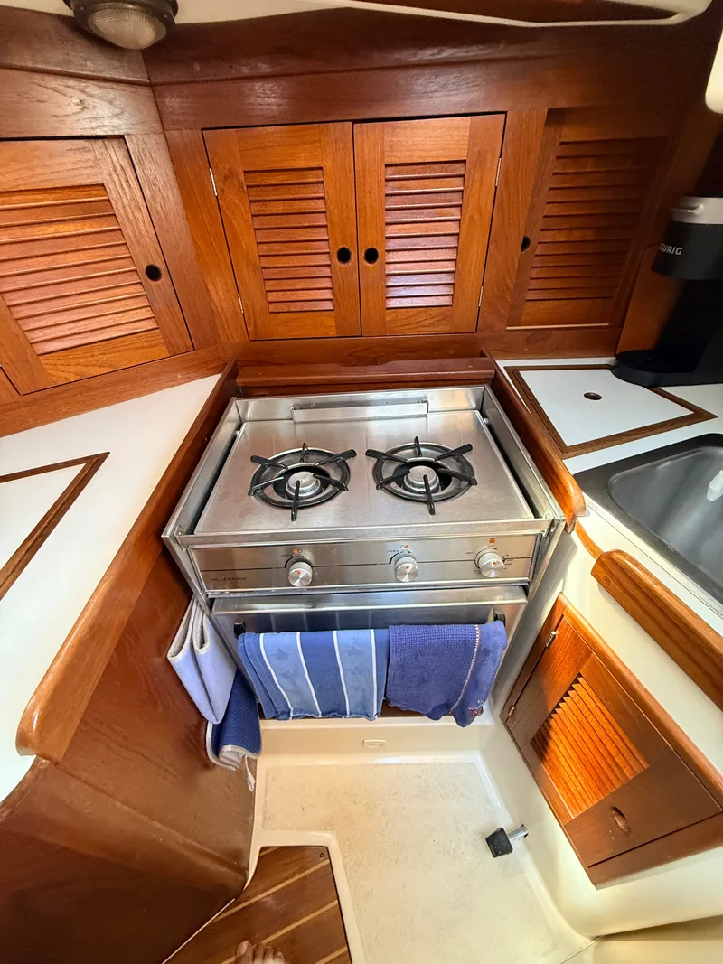 Slide: The Image of The galley of a 1992 Tartan T 31 with a two-burner stove and wooden cabinets. - 18