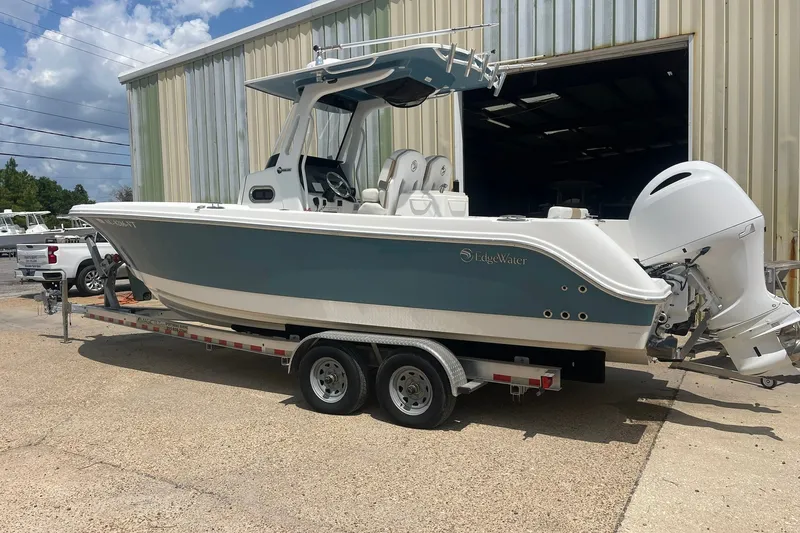 Slide: The Image of 2023 Edgewater 262CC boat on trailer, parked outside a warehouse. - 1