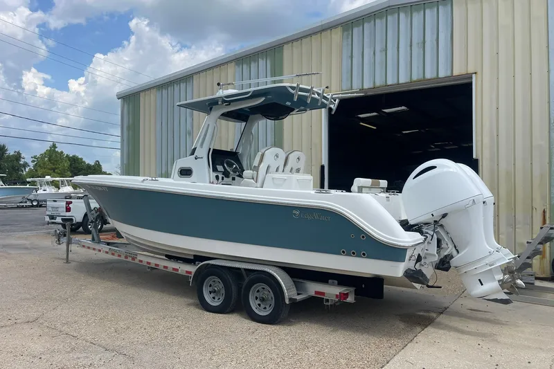 Slide: The Image of 2023 Edgewater 262CC boat on trailer outside a large garage. - 18