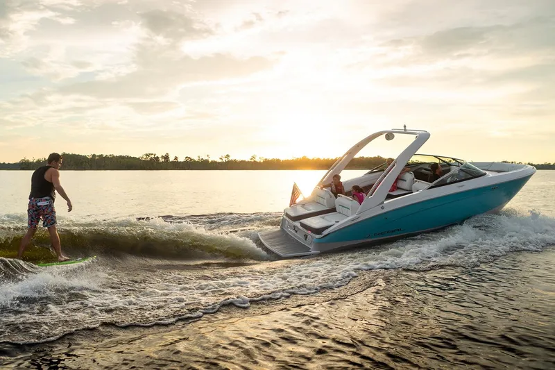 Slide: The Image of Manufacturer Provided Image: 2026 Regal LS4 Surf boat creating waves at sunset with a wakeboarder. - 3