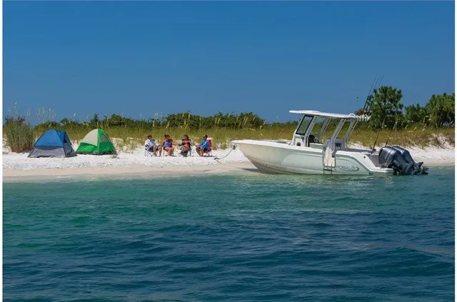Slide: The Image of A 2021 Robalo R272 Center Console boat is anchored by the beach. People are camping nearby. - 16