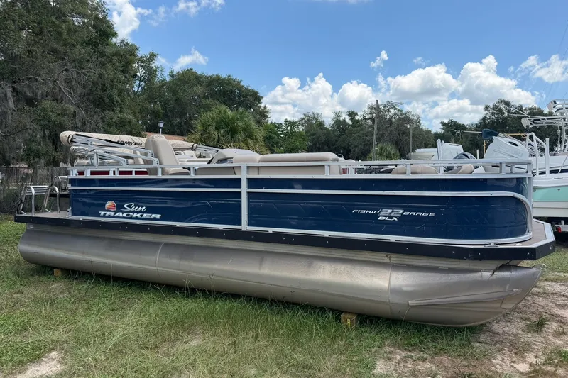 The Image of 2025 Sun Tracker Fishin' Barge 22 DLX pontoon boat on grassy area under blue sky. - 0