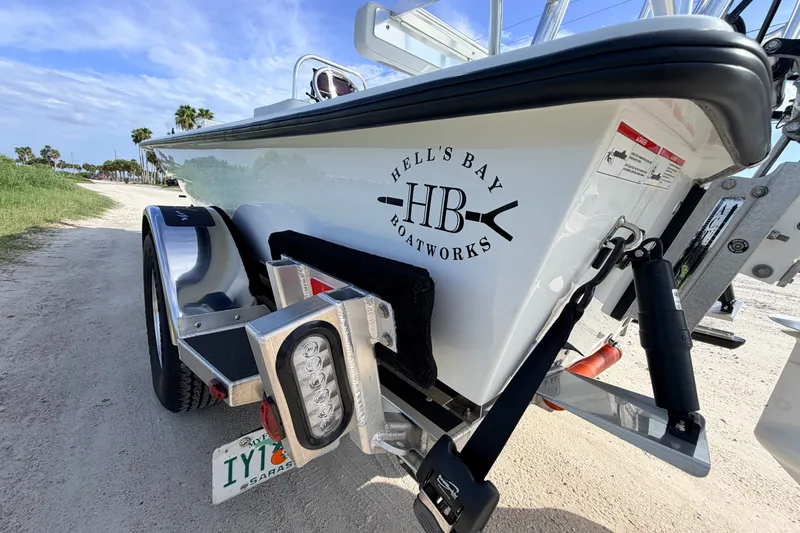 Slide: The Image of 2021 Hell's Bay Marathon boat on trailer, featuring logo and license plate, parked on sandy road. - 20